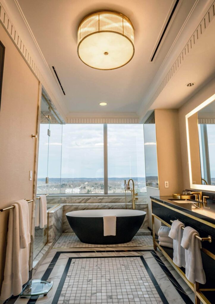 Things to Do at Mohegan Sun: Where to Eat, Stay, and Play. Luxurious bathroom with a black bathtub, large window view, and modern gold fixtures.