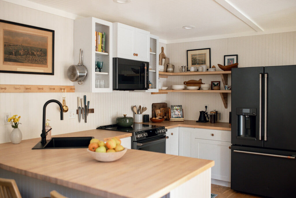Modern kitchen with black appliances, wooden countertops, open shelves, and a bowl of apples on the counter.