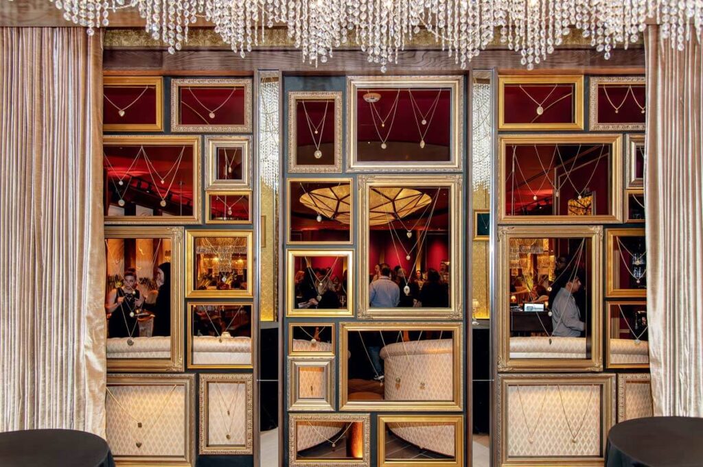 Luxurious lounge with mirrored panels, chandeliers, and people mingling in an elegant, warmly lit space.