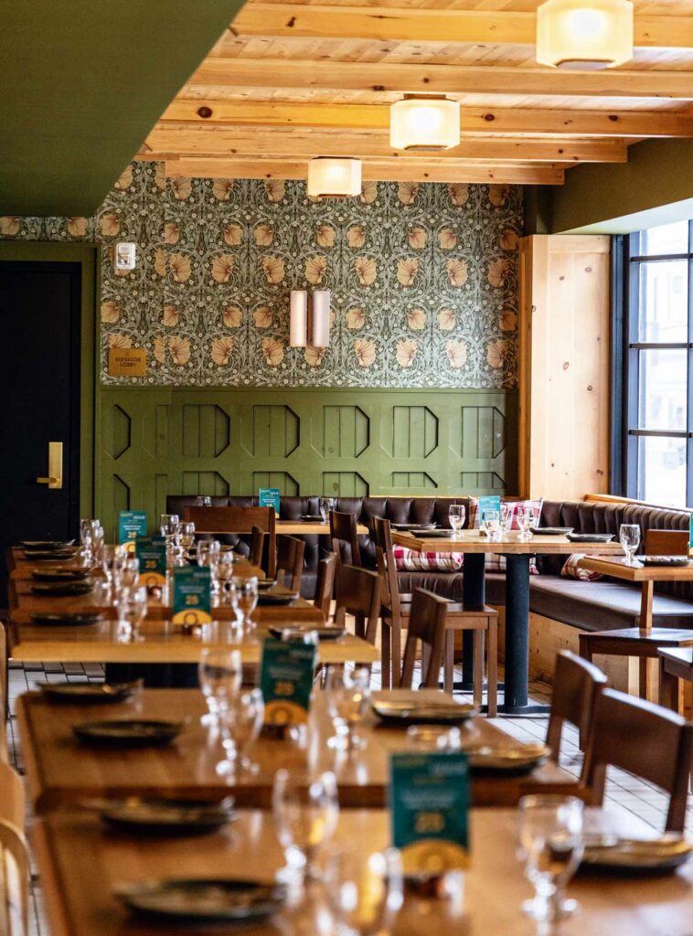 A cozy restaurant dining area with wooden tables, set with plates and glasses, and patterned wallpaper.