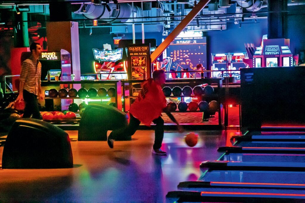 Things to Do at Mohegan Sun: Where to Eat, Stay, and Play. Person bowling in a neon-lit arcade with arcade games and bowling balls visible in the background.