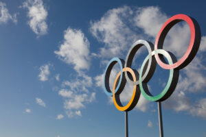 Olympic rings sculpture against a blue sky with scattered clouds.