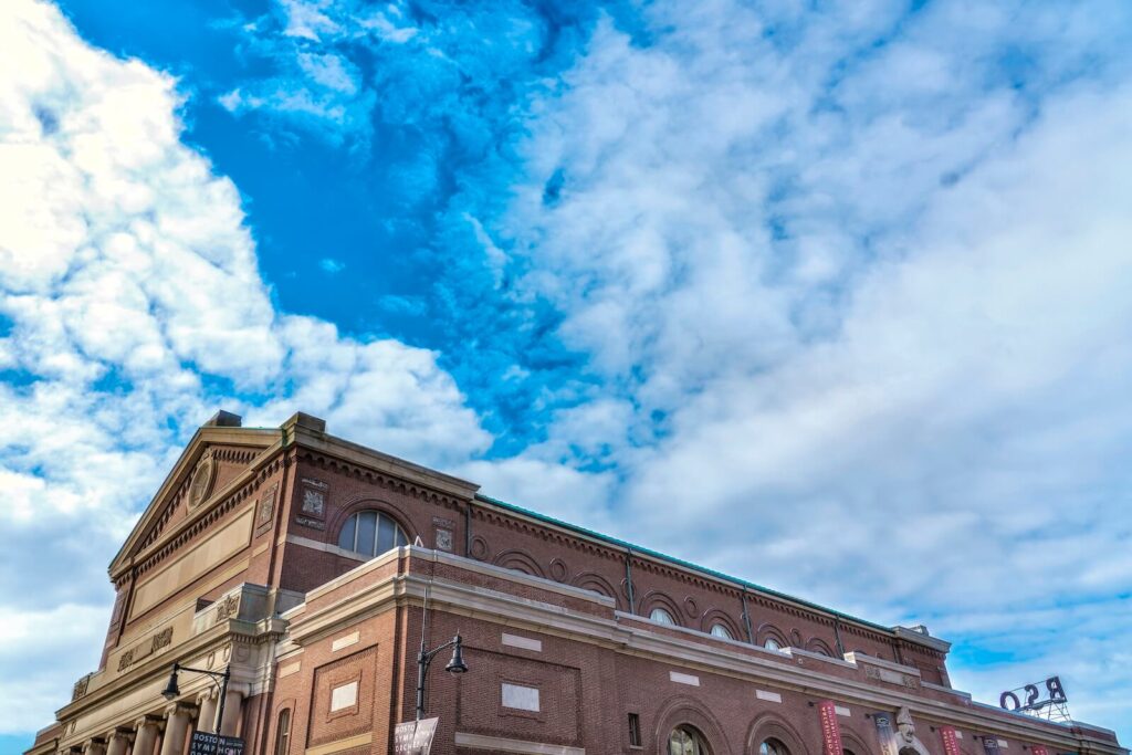 A large brick building with columns beneath a bright blue sky filled with scattered clouds.
