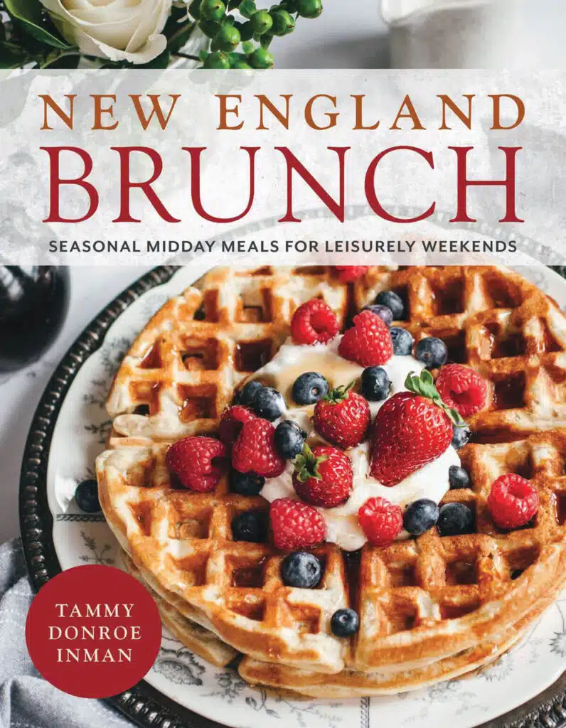 A plate of waffles topped with whipped cream and berries, featured on the cover of "New England Brunch" cookbook.