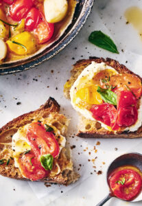 Groundswell Café’s Tomato Tartines. Toasted bread topped with burrata cheese, roasted tomatoes, and fresh basil on parchment paper.