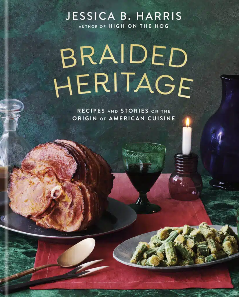 Book cover for "Braided Heritage" shows a lit candle on a green and red table setting with sliced ham on a platter, fried okra in a serving dish, and drinks.