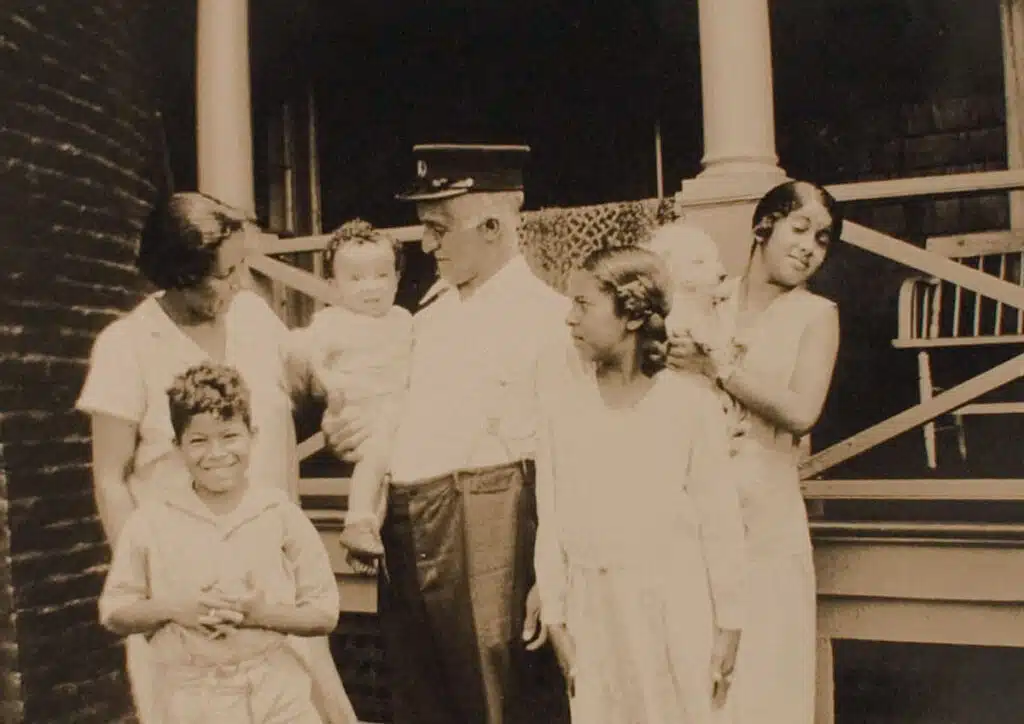 Vintage photo of a family of six, smiling and standing together on a wooden porch.
