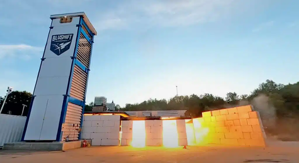 A rocket engine test fires near concrete barriers at a bluShift Aerospace facility, with flames visible.