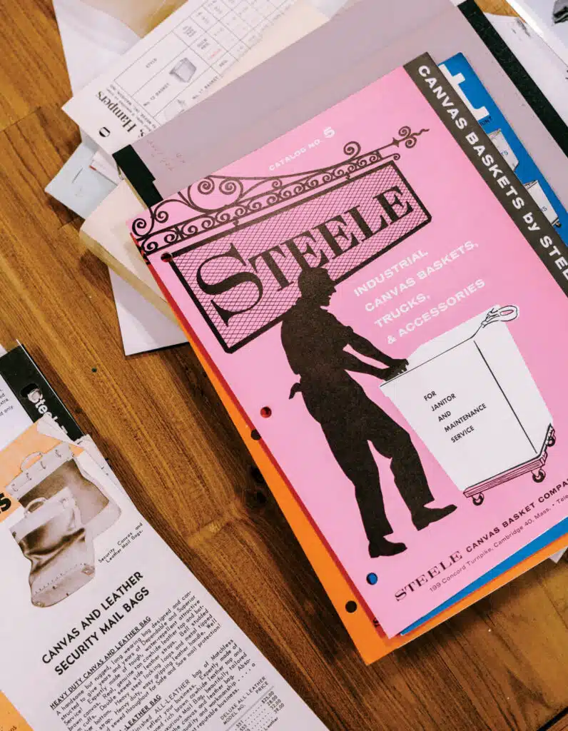 A pink Steele catalog with a worker graphic lies on a table among scattered papers and brochures.