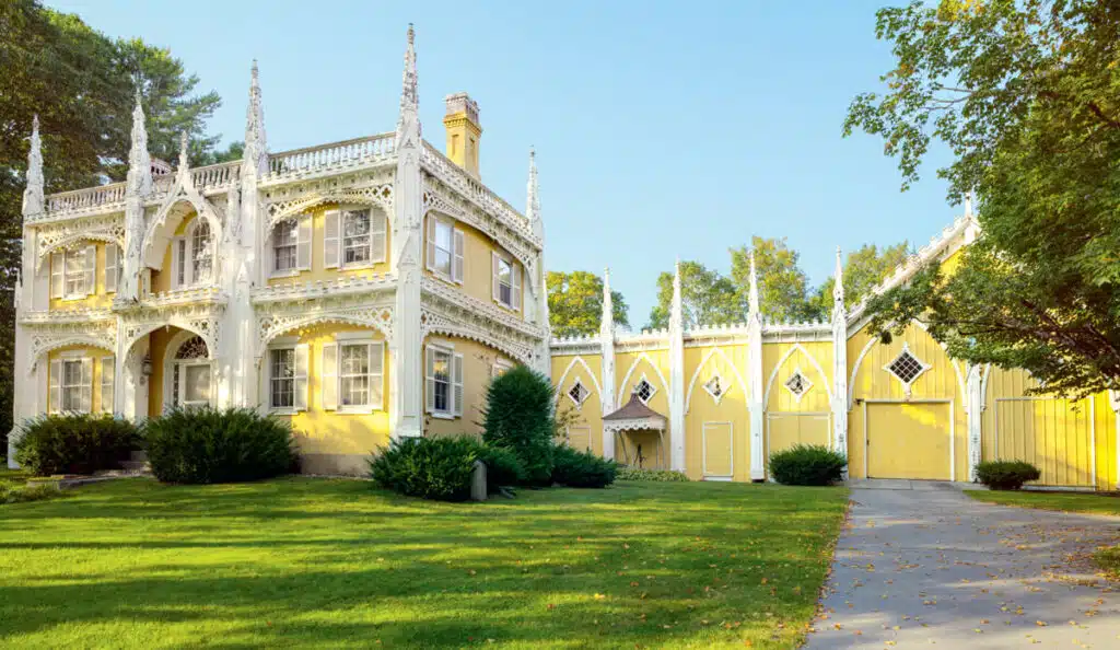 Yellow Gothic-style house with ornate white trim and large green lawn on a sunny day; an example of gingerbread houses.