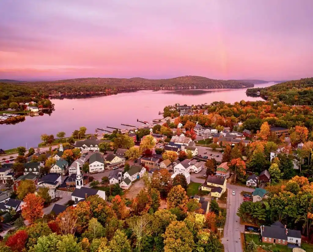Aerial view of a lakeside town with colorful autumn trees and a pink sunset sky.