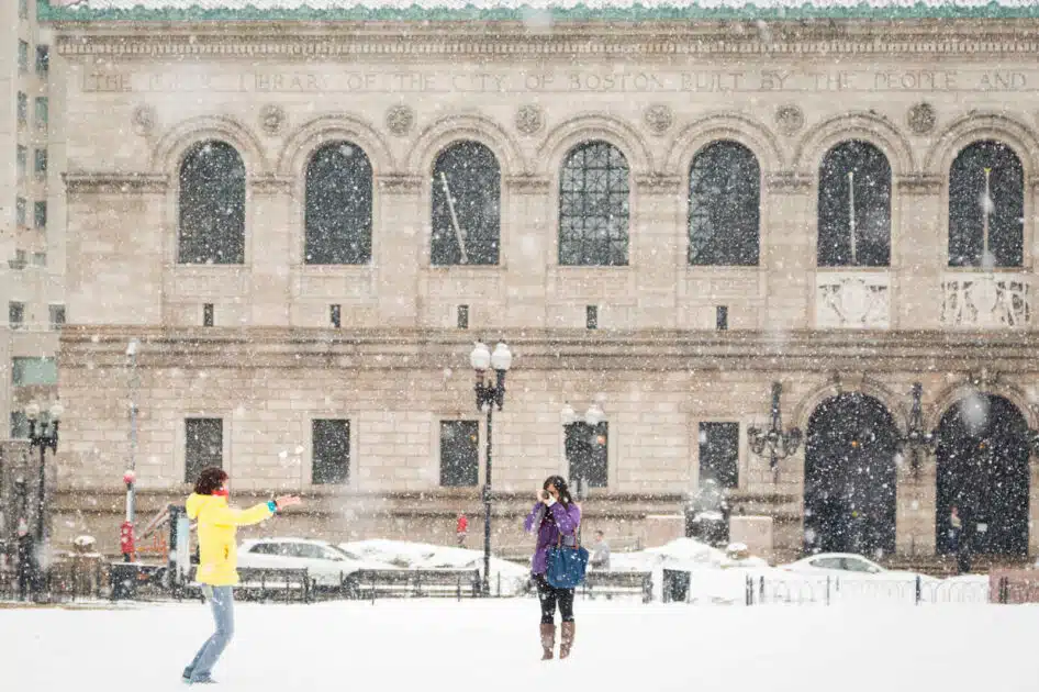 Two people play in the snow in front of the Boston Public Library on a snowy day.