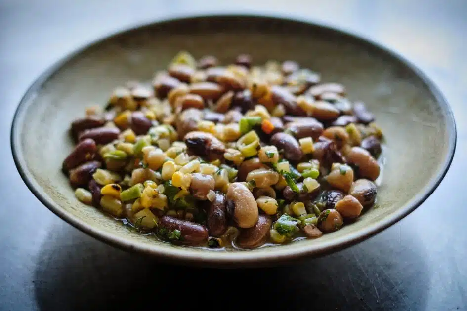 A bowl of mixed bean salad with corn, chopped herbs, and vegetables on a rustic plate.