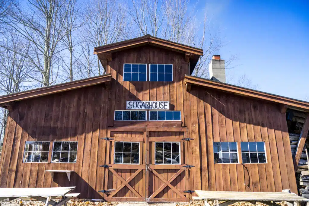 A rustic wooden sugarhouse with large windows and a sign reading "SUGARHOUSE" on the front.