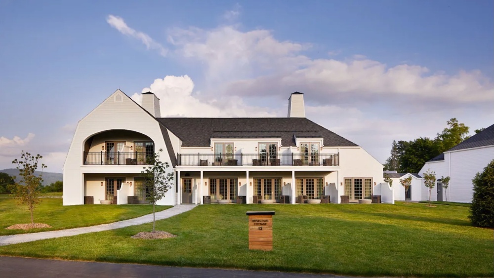 Two-story white building with balconies, large windows, and a manicured lawn under a blue sky.