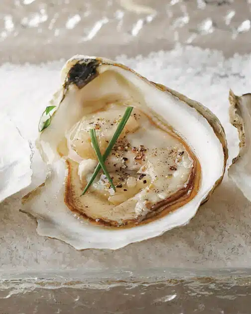 An oyster on the half shell garnished with chives and mignonette sauce, served on a bed of coarse salt.