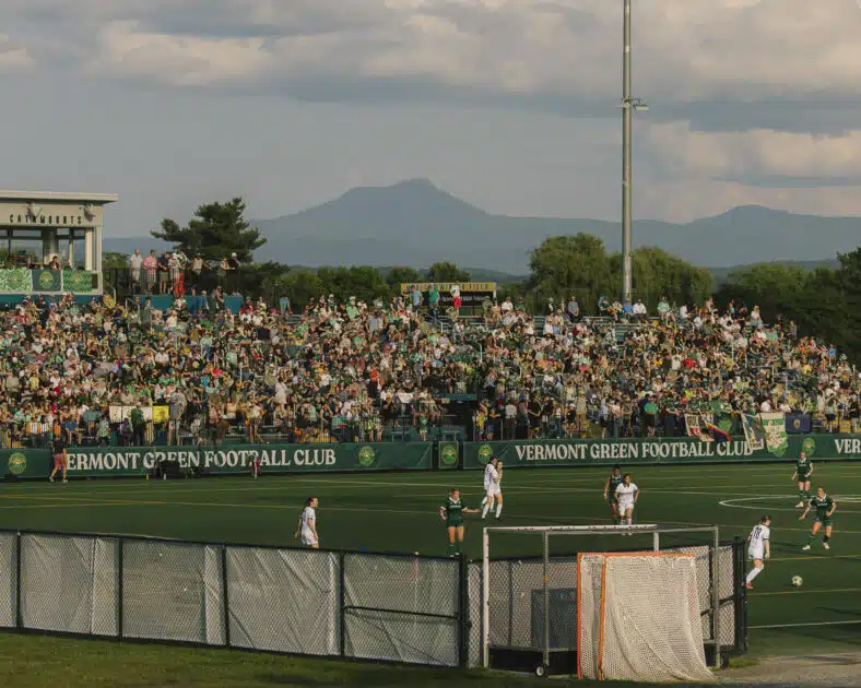 A soccer match at Vermont Green FC stadium with a large crowd and mountains in the background.