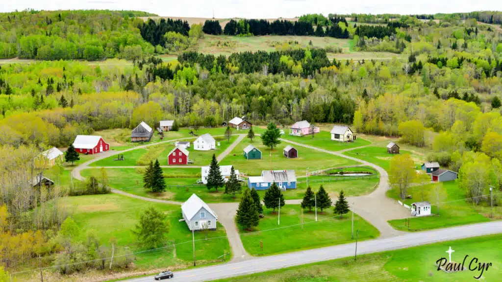 Aerial view of a small rural village with houses, barns, trees, and a winding road in spring.