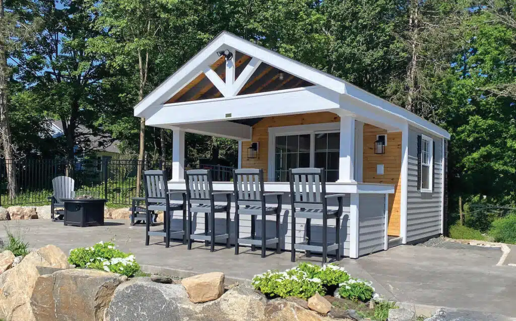 Small poolside bar shed with a covered patio, high chairs, and surrounded by greenery and rocks.