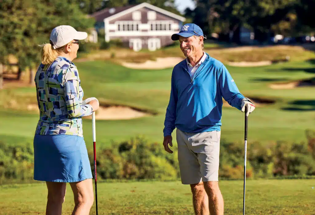 Two people with golf clubs chat and smile on the golf course at Ocean Edge Resort on Cape Cod.