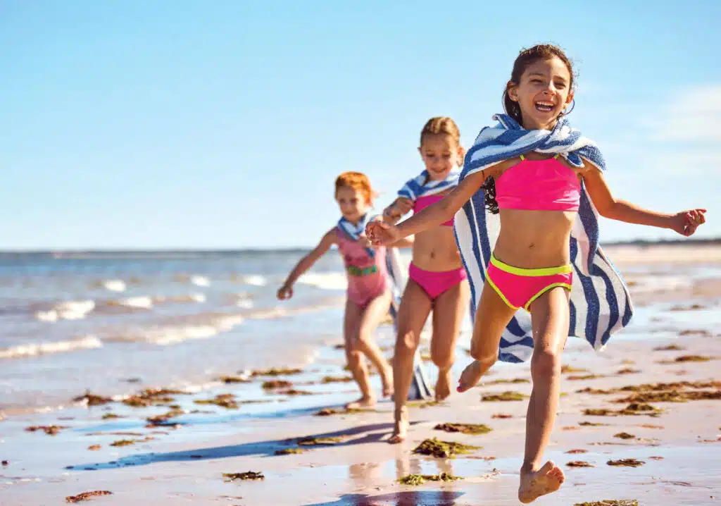 Three happy children in swimsuits run along the private beach at Ocean Edge Resort on Cape Cod.