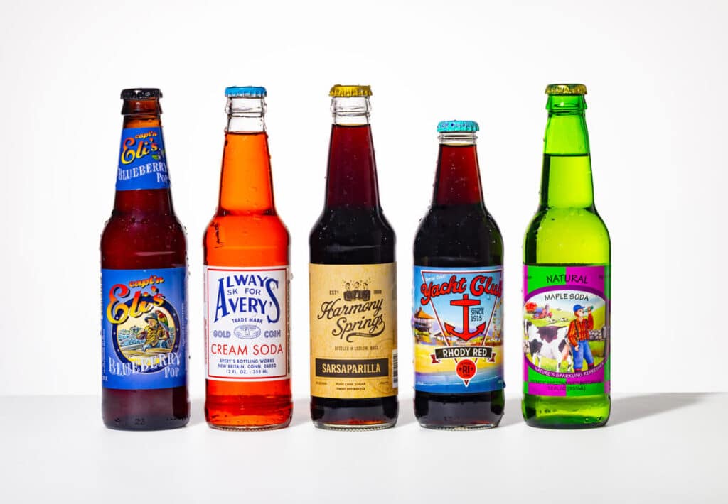 Five assorted colorful soda bottles standing in a row on a white surface with various labels visible.