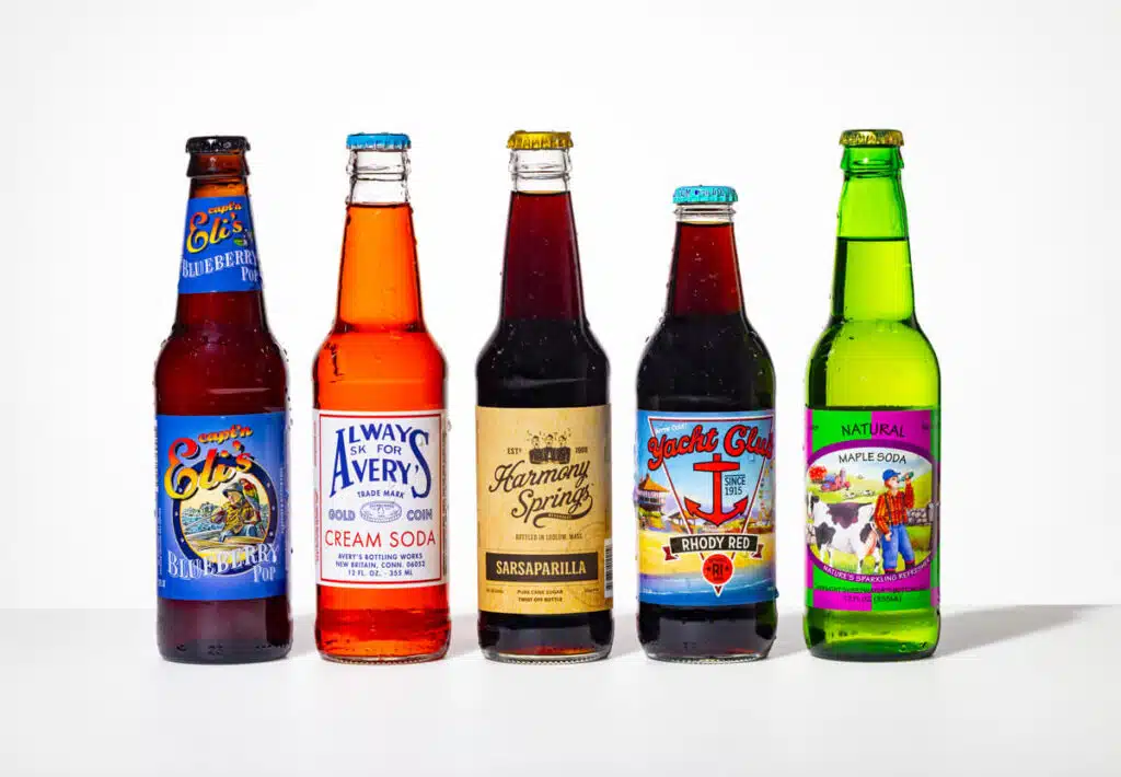 Five assorted colorful soda bottles standing in a row on a white surface with various labels visible.