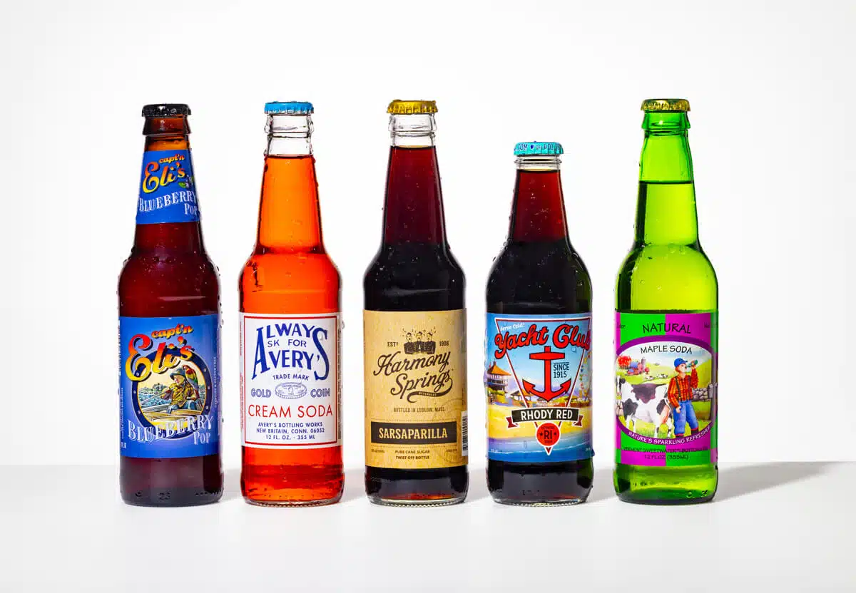 Five assorted colorful soda bottles standing in a row on a white surface with various labels visible.