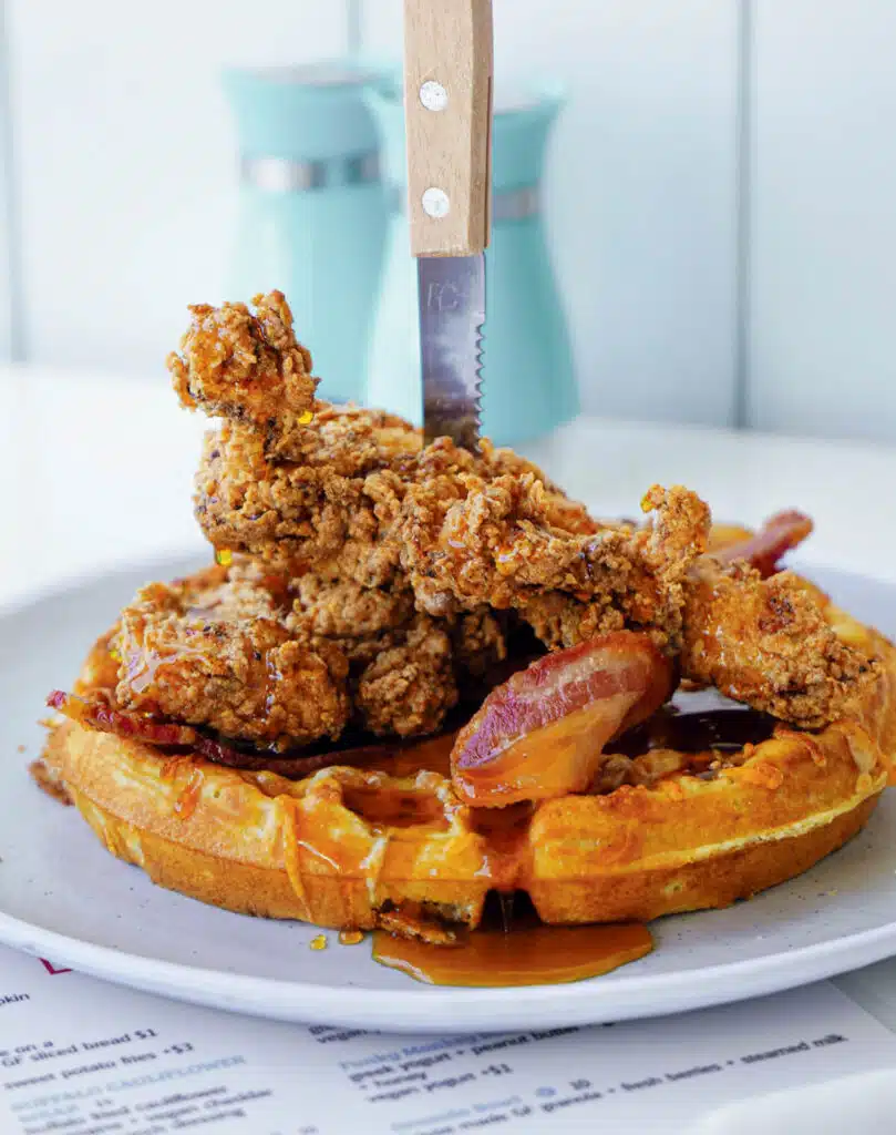2026 Connecticut Travel Guide | Hotels, Dining & Attractions. A plate of fried chicken and bacon on a waffle, topped with syrup and a knife stabbed in the center.