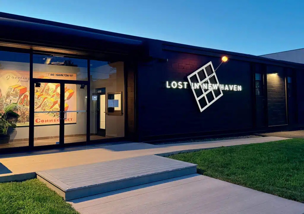Modern building with a "Lost in New Haven" sign and a colorful mural inside, seen at dusk.