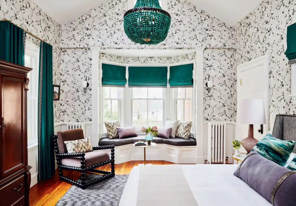 2026 Rhode Island Travel Guide. Bright bedroom with floral wallpaper, green chandelier, bay window seat, and teal curtains.