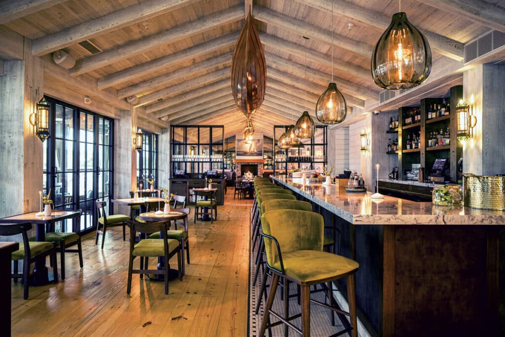 Chic, modern restaurant with wooden floors, marble bar, green chairs, and large glass pendant lights.