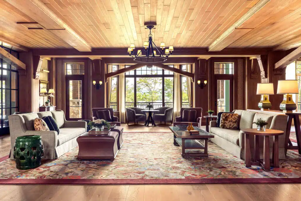 Cozy lodge-style living room with sofas, armchairs, large windows, and a patterned rug on wooden floors.