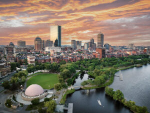 A city skyline at sunset with a river, park, and dome-shaped building in the foreground.