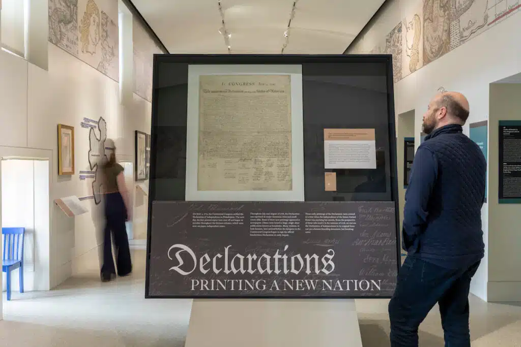 A man views a framed historical document titled "Declarations: Printing a New Nation" in a museum exhibit.