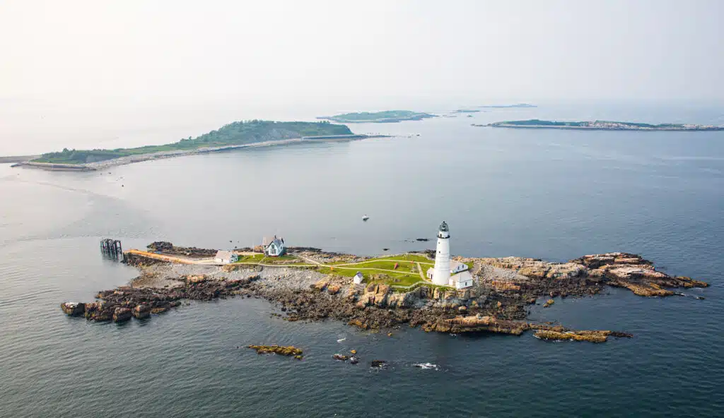 Aerial view of a small rocky island with a lighthouse and buildings surrounded by calm ocean waters.