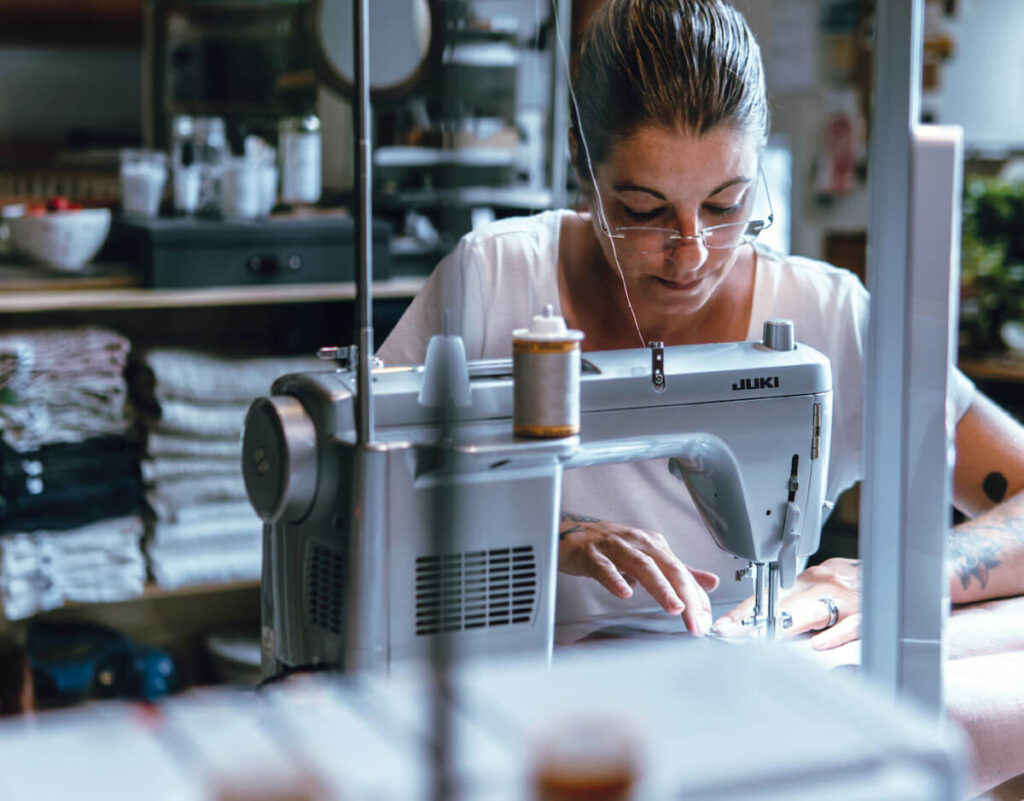 A woman uses a sewing machine in a workshop, focusing intently on her work.