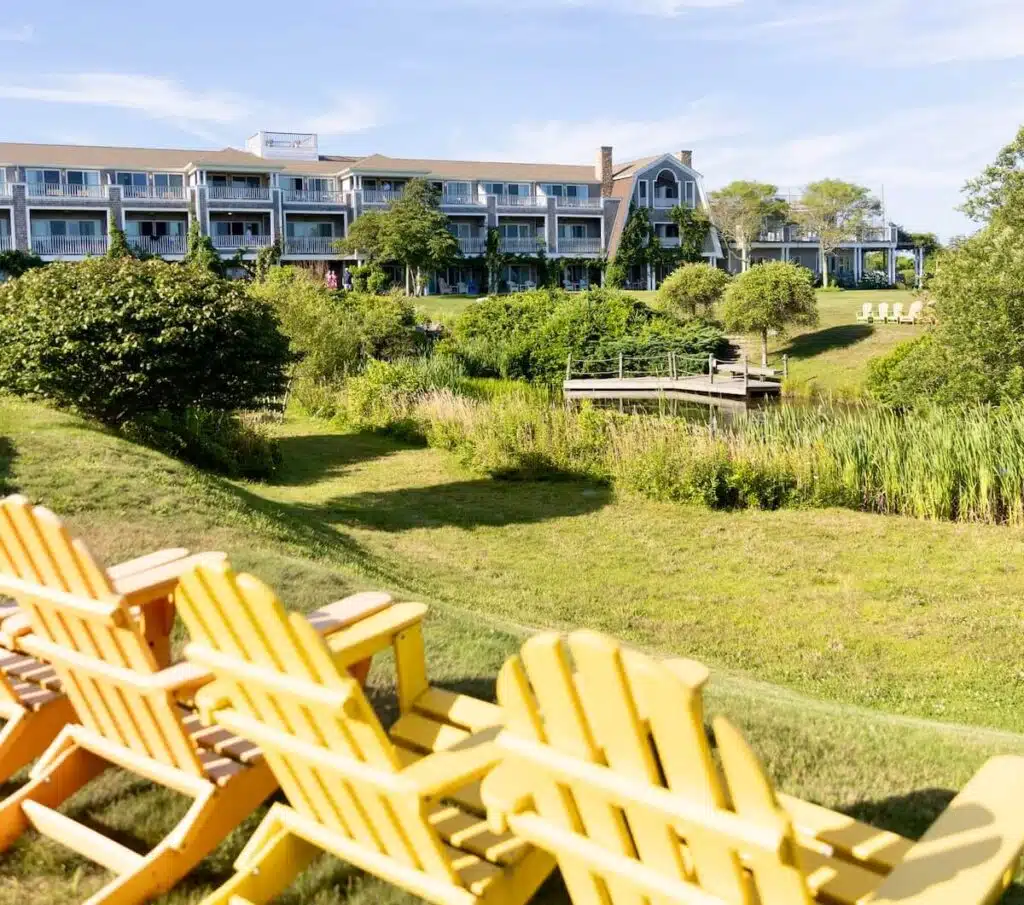 Yellow Adirondack chairs on a grassy hill facing a large hotel and lush green landscaping under a blue sky.