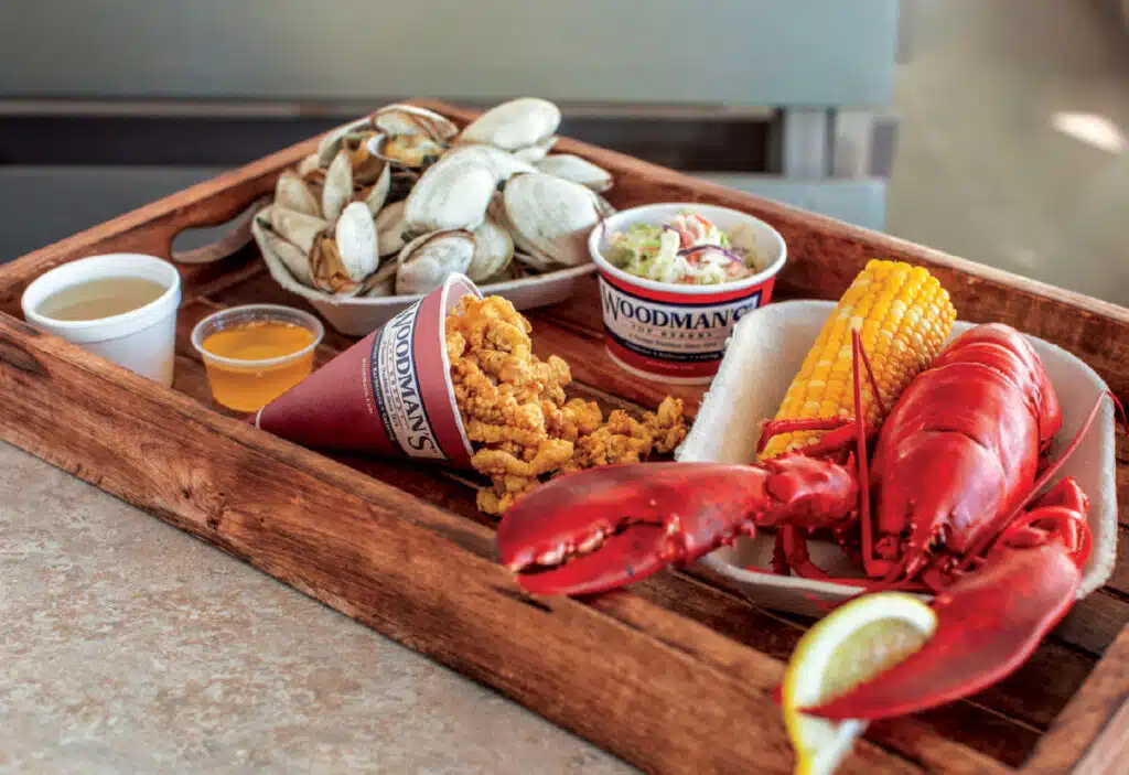 Wooden tray with lobster, clams, corn, fried seafood, coleslaw, and dipping sauces on a table.