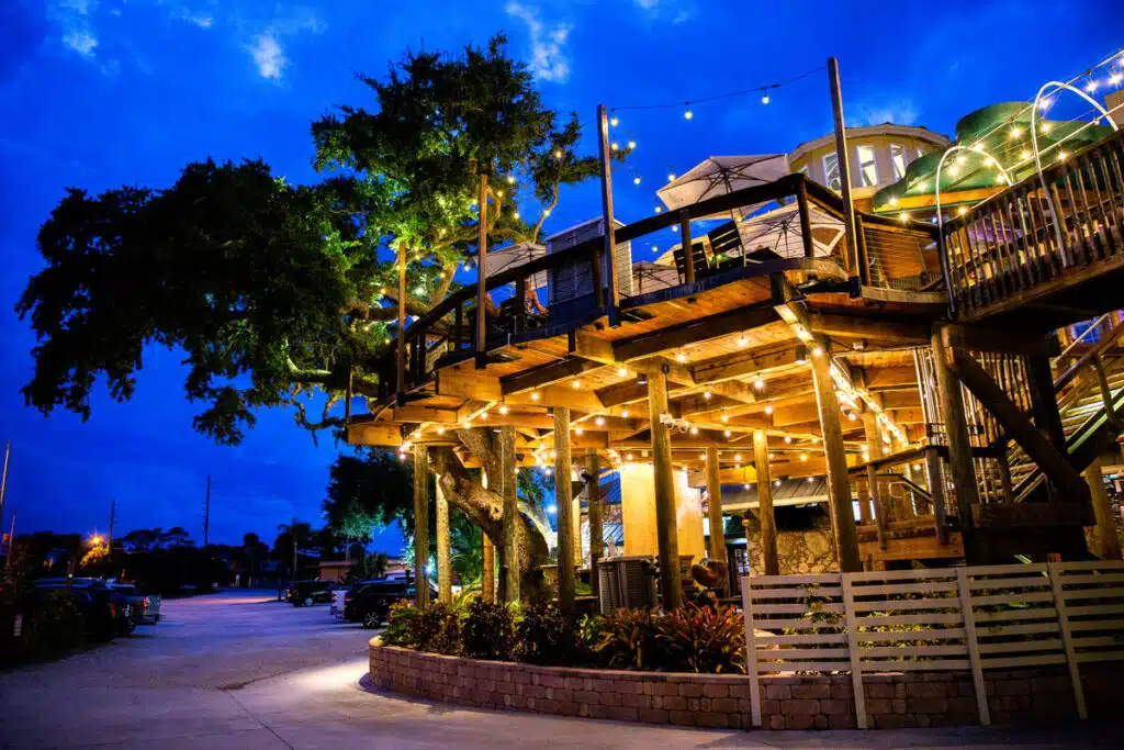 Norwood's Treehouse Restaurant in New Smyrna Beach with string lights, trees, and a vibrant blue evening sky.
