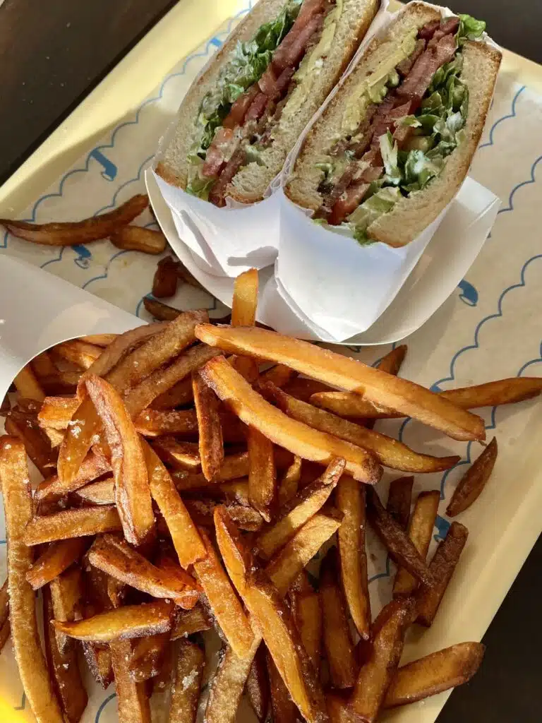 A sandwich at Paco Submarine with lettuce, tomato, bacon, and fries on a yellow tray.