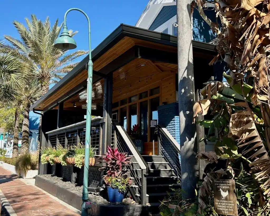 Third Wave New Smyrna Beach restaurant exterior with large windows, tropical plants, and steps leading to the entrance on a sunny day.