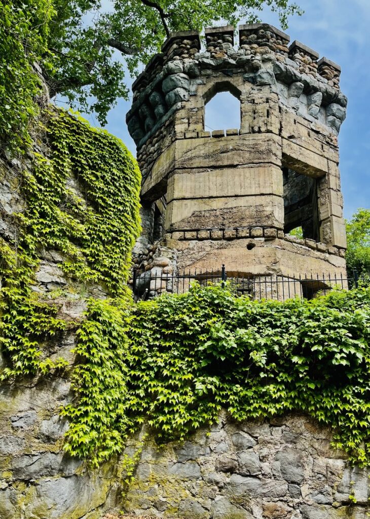 Bancroft's Castle on Gibbet Hill in Groton, MA. Old stone tower with large windows, surrounded by green ivy climbing up the rocky wall beneath it.