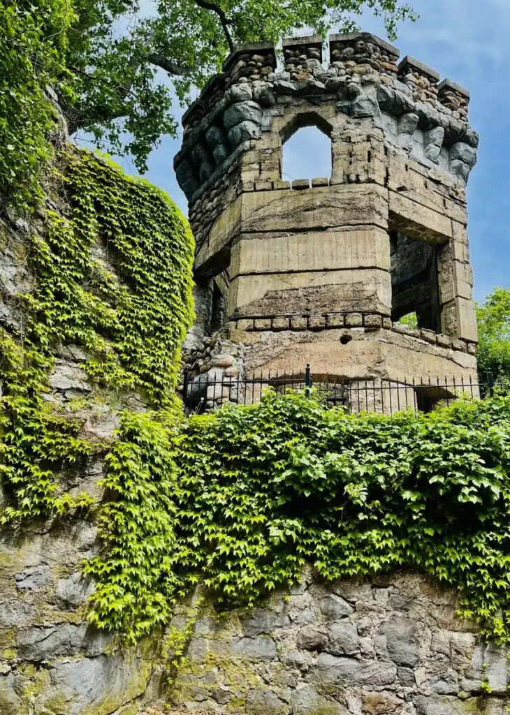Bancroft's Castle on Gibbet Hill in Groton, MA. Old stone tower with large windows, surrounded by green ivy climbing up the rocky wall beneath it.