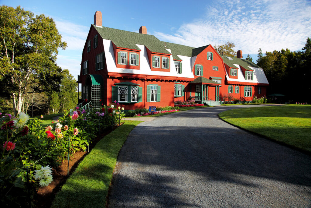 A large red house with white trim, green roof, and a curved driveway, surrounded by gardens and trees.