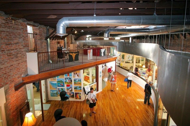 Hub on Canal interior with brick walls, wooden floors, art displays, and visitors walking and viewing exhibits in New Smyrna Beach, Florida.