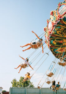 People on a colorful swing ride at an amusement park, legs outstretched, enjoying a sunny day.
