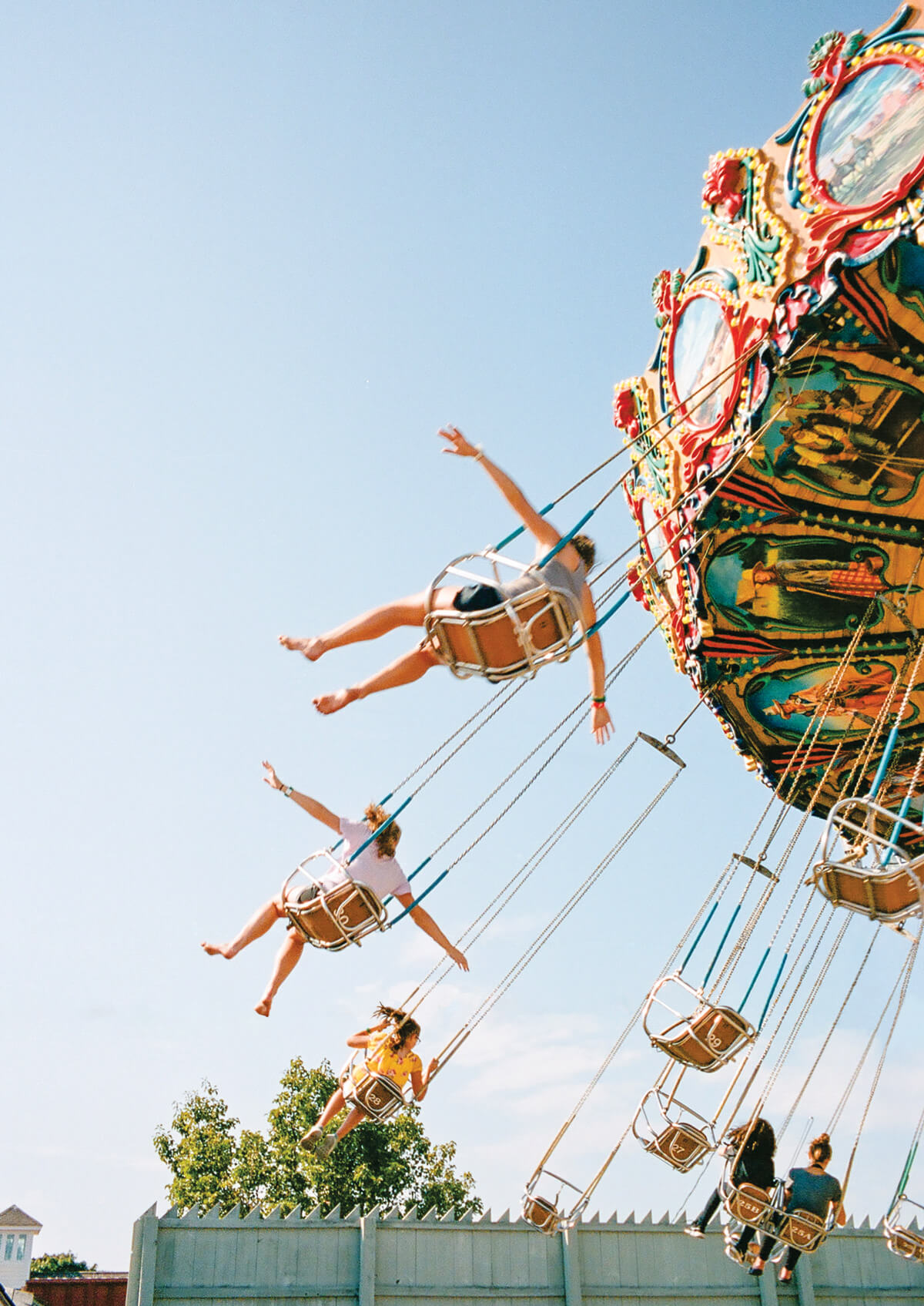 People on a colorful swing ride at an amusement park, legs outstretched, enjoying a sunny day.