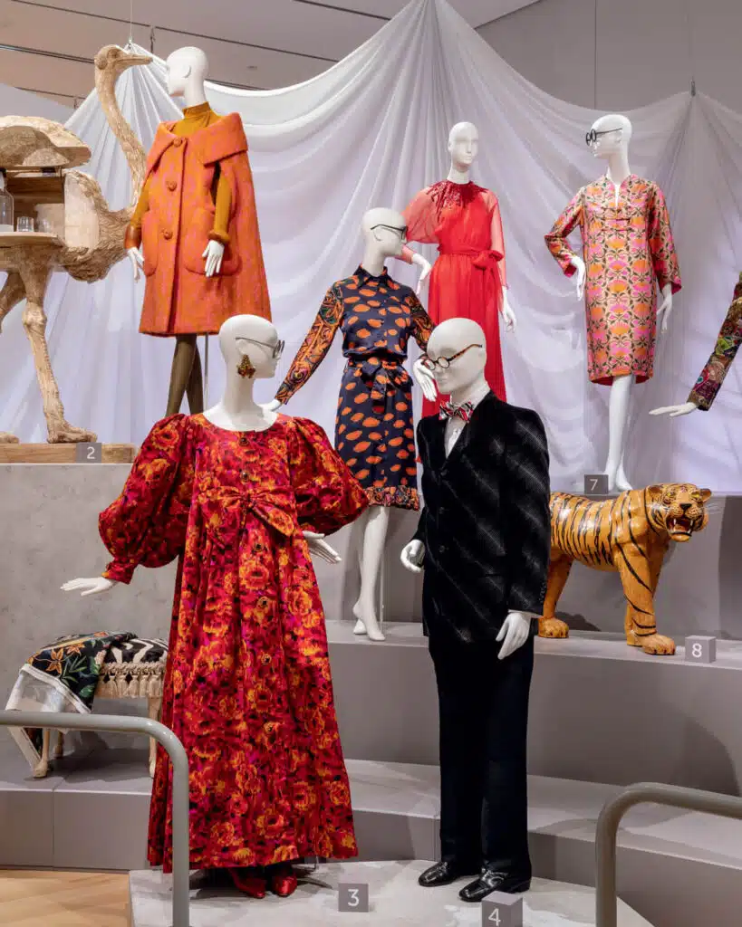 Mannequins in vibrant vintage clothing stand near animal props with white draped fabric in the background.