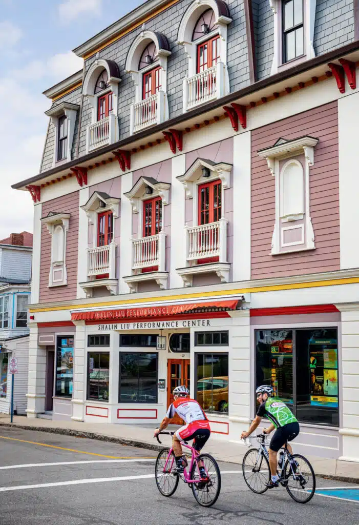 Two cyclists ride past the Shalin Liu Performance Center, a historic building with ornate windows and balconies.